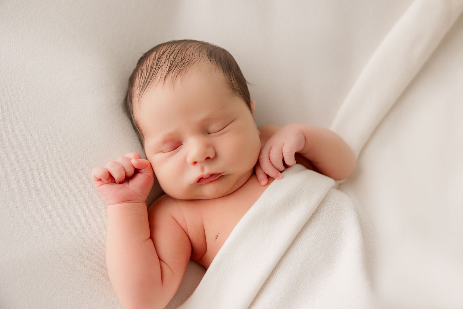 Peaceful sleeping newborn wrapped in white blanket during professional photography session.