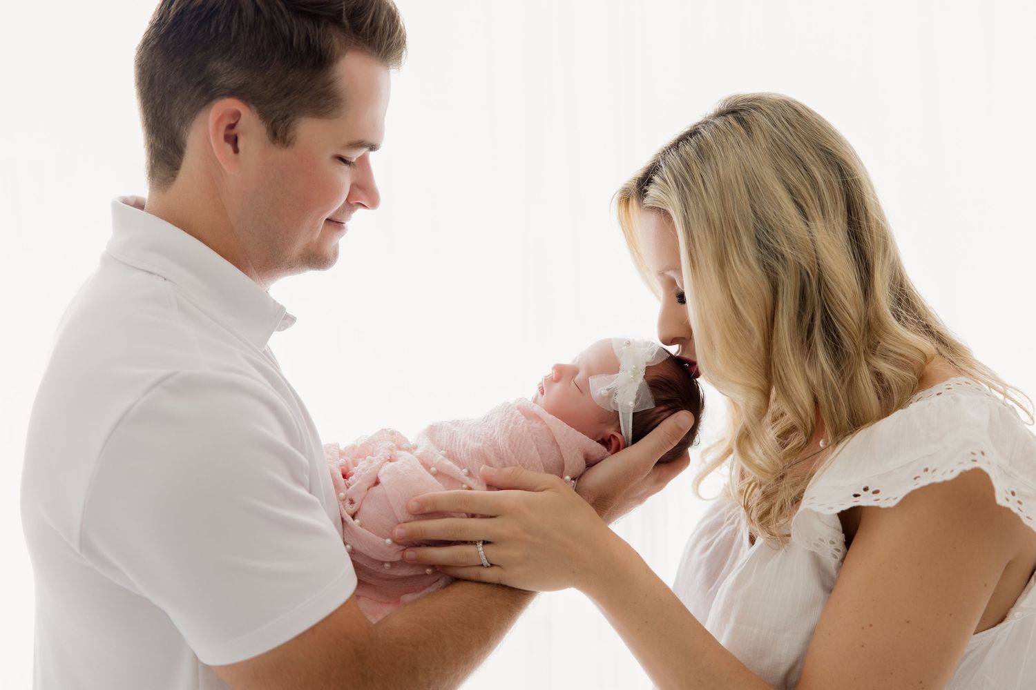 Family with newborn baby cuddle together during intimate lifestyle photography session in bright studio setting.