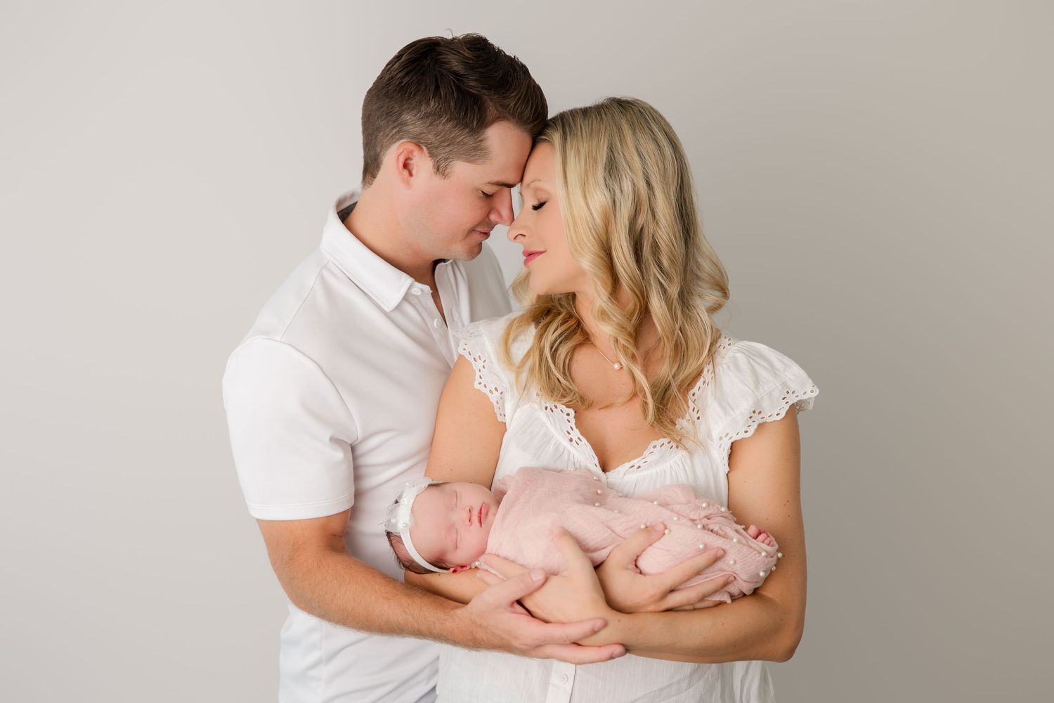 A romantic couple dressed in white embraces on a light gray backdrop during an intimate photography session.