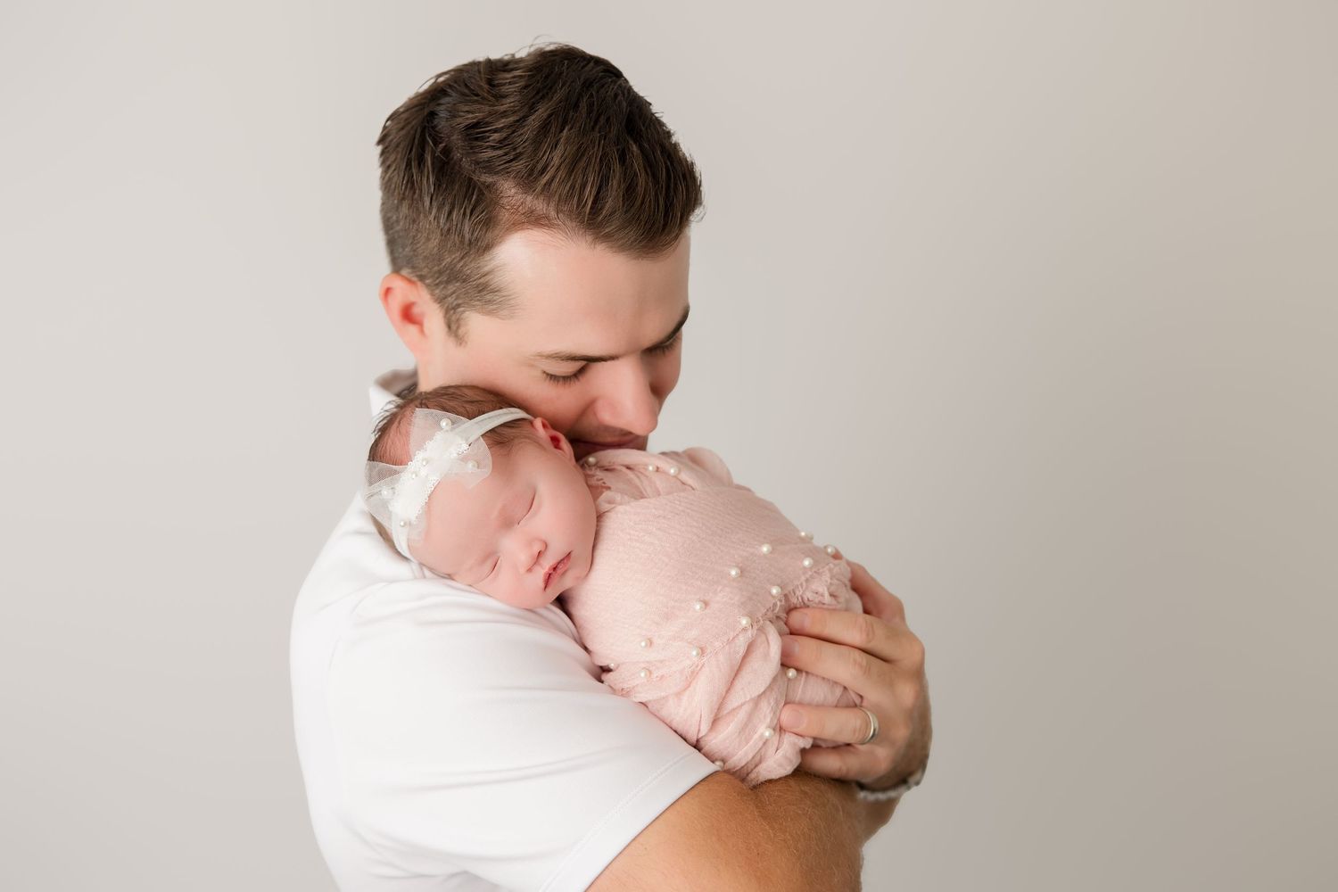 Parents share tender moments with their newborn baby during studio photoshoot on light backdrop.