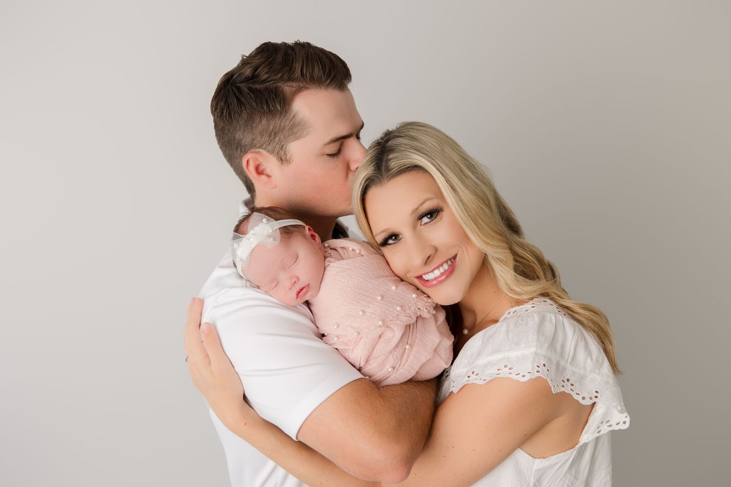 A tender moment between a couple wearing white as they lean close together against a neutral background.