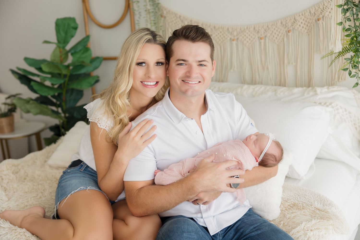 Family poses on white couch with newborn baby during professional lifestyle photography session.