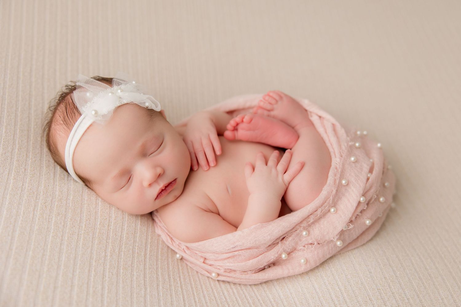 Sleeping newborn baby wrapped in pink swaddle during professional studio photography session.