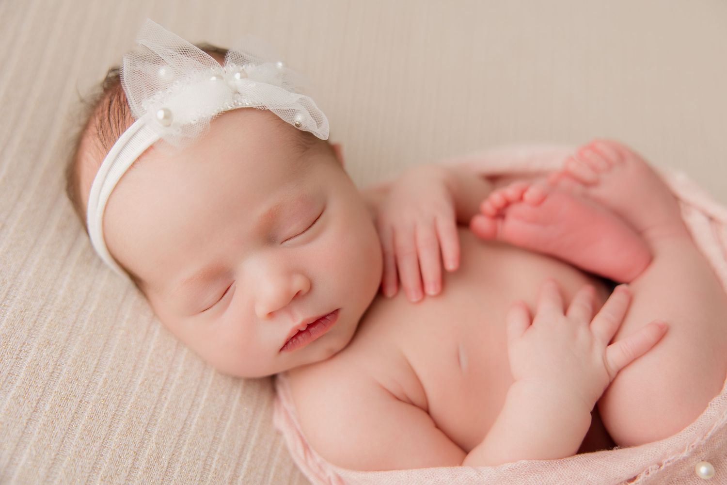 A serene newborn baby swaddled in soft white fabric sleeps peacefully during a professional photography session.