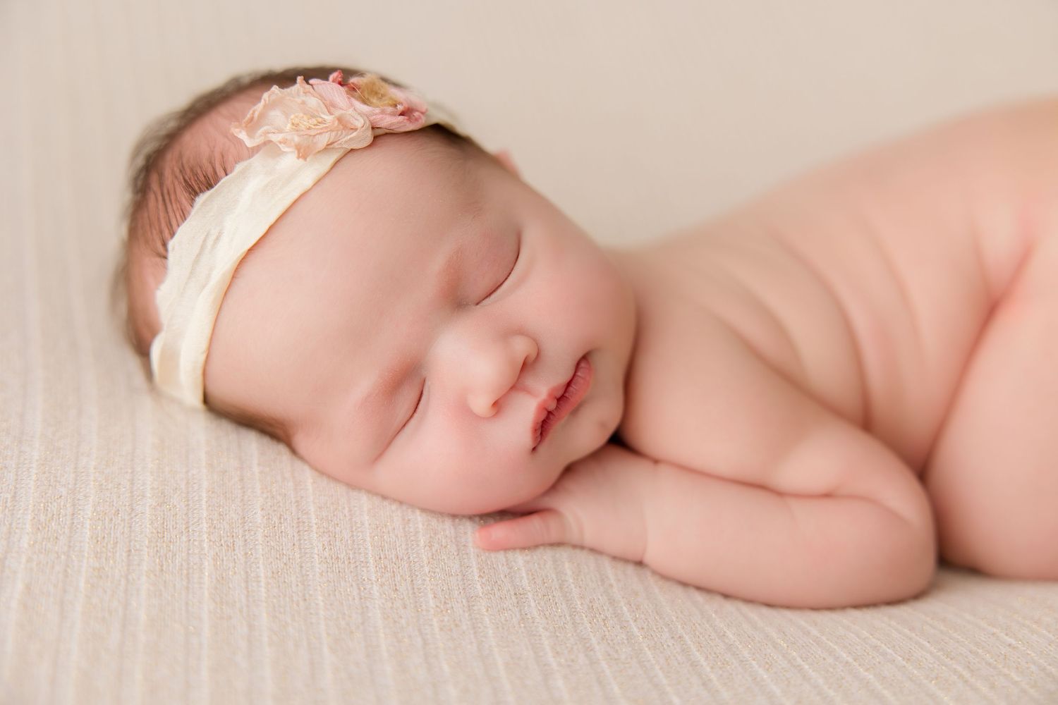 A sleeping newborn baby lies peacefully on soft white fabric during a professional photo session.