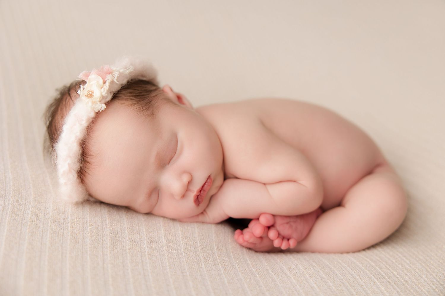 Sleeping newborn baby lying on textured cream blanket in professional studio setting.
