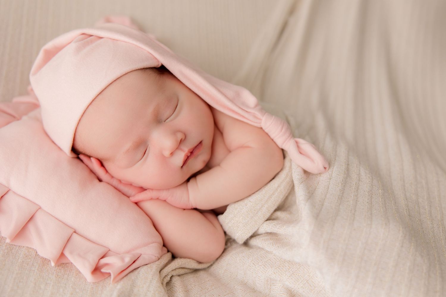 Sleeping newborn wrapped in pink fabric during professional portrait session on cream background.