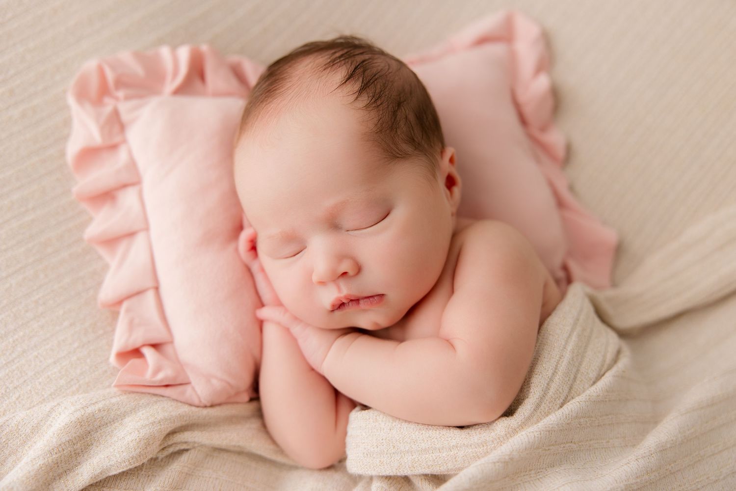 Peaceful sleeping newborn baby wrapped in soft pink fabric laying on white textured surface.