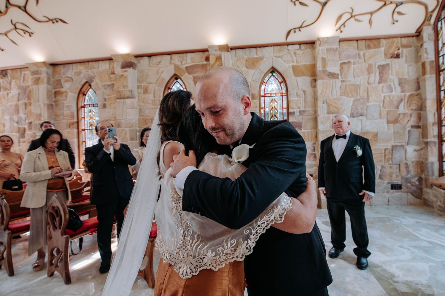 Wedding couple shares their first dance in a rustic stone chapel while guests watch from the sides.