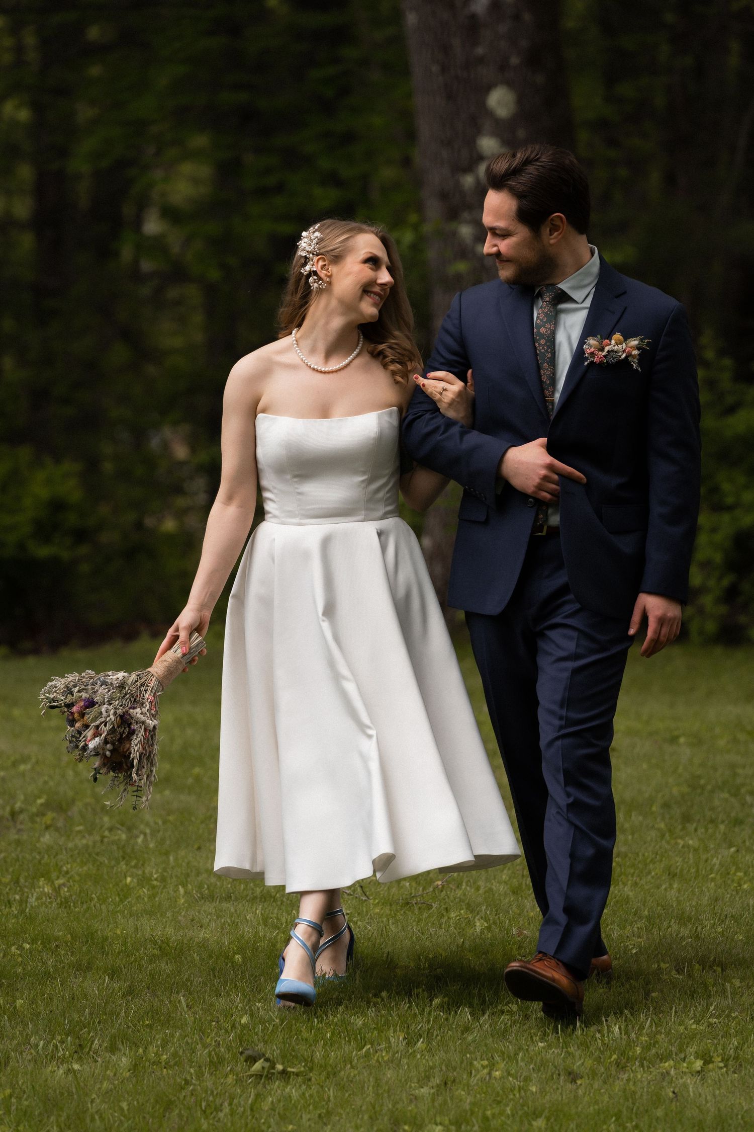 A bride and groom enjoy a playful moment with their dog in a grassy outdoor setting.