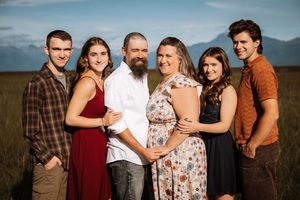 Family of six pose together outdoors with mountains in the background at sunset.