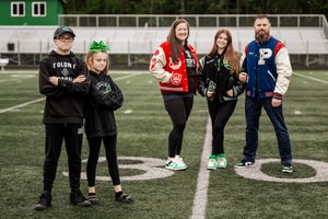 Family of 5 posing on a football field wearing their lettermen jackets and school colors.