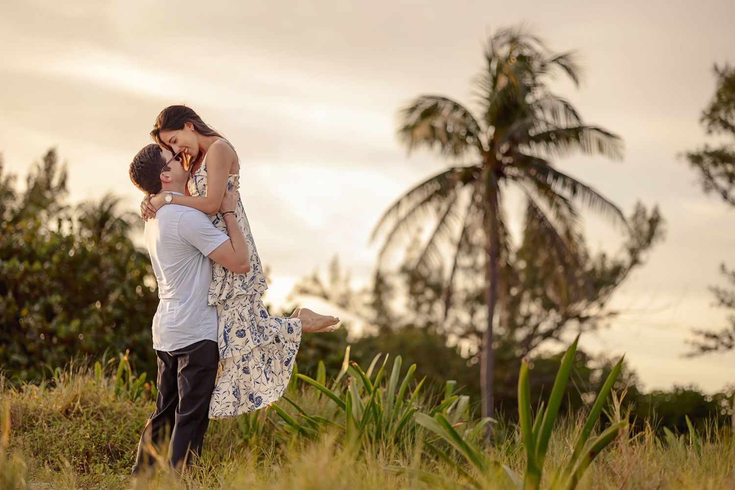 A romantic sunset moment captured on a grassy hill with palm trees silhouetted against the warm sky.