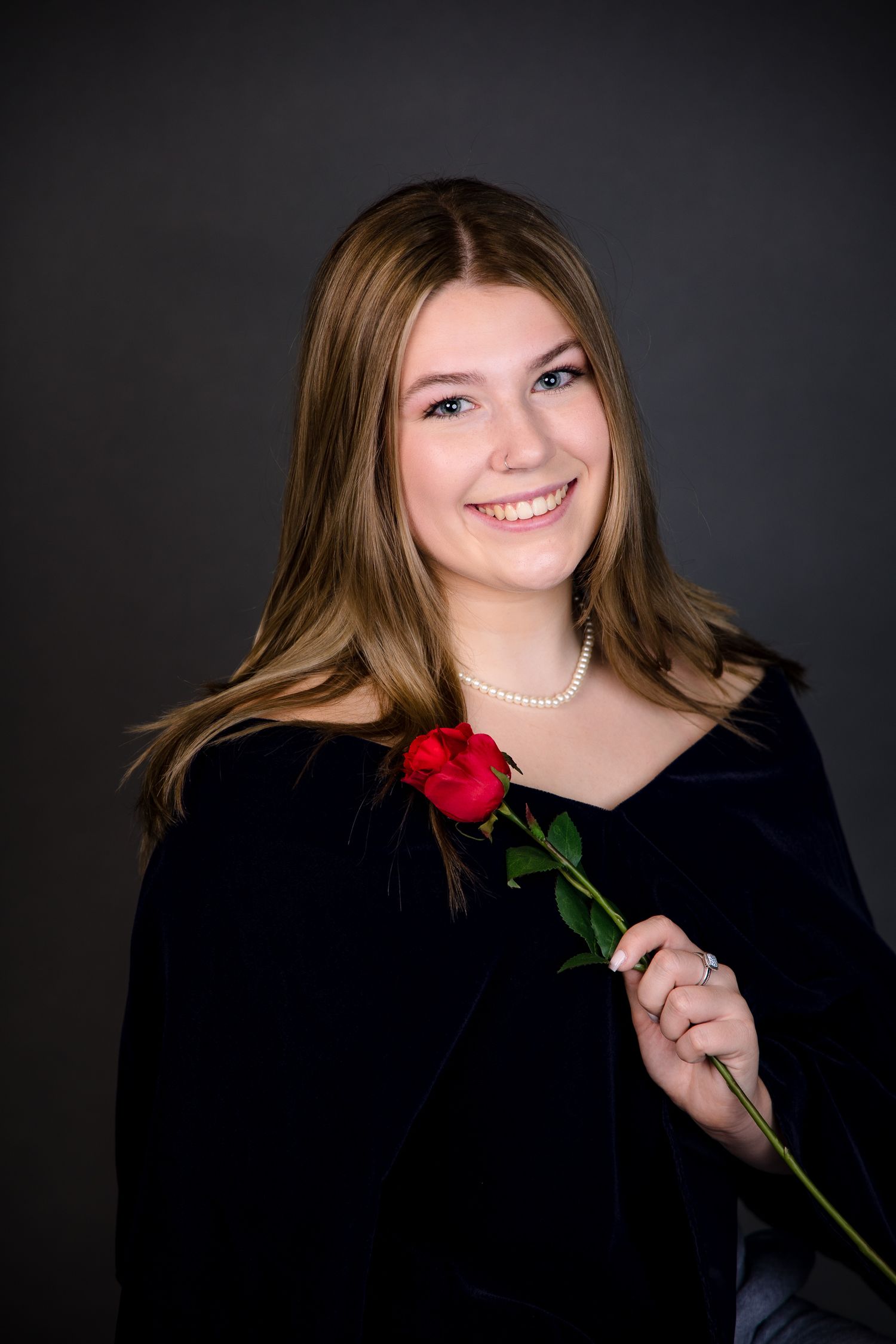 Two graduates in bright red gowns share a joyful moment under green foliage during a graduation photoshoot.
