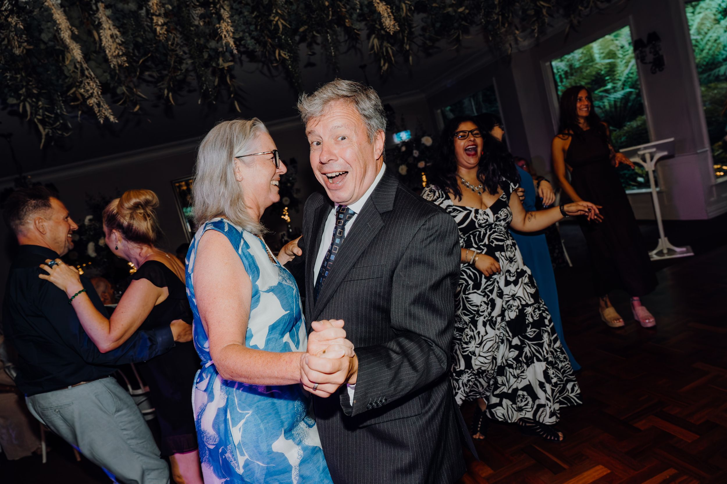 People dancing together at an evening event in formal attire on a dark dance floor.