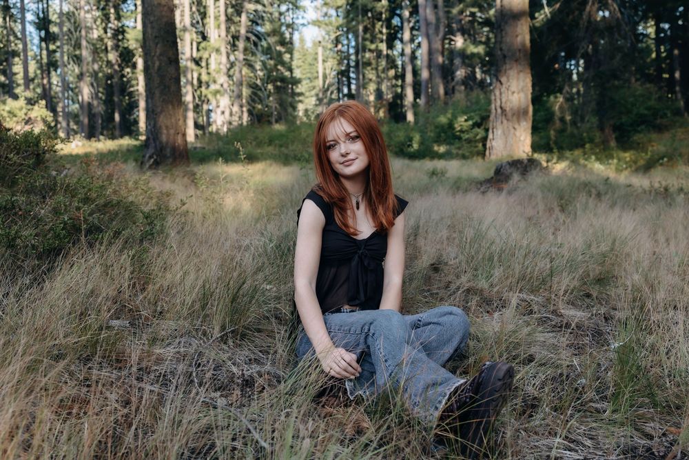 Outdoor portrait session in tall grass with sunlit forest in background.