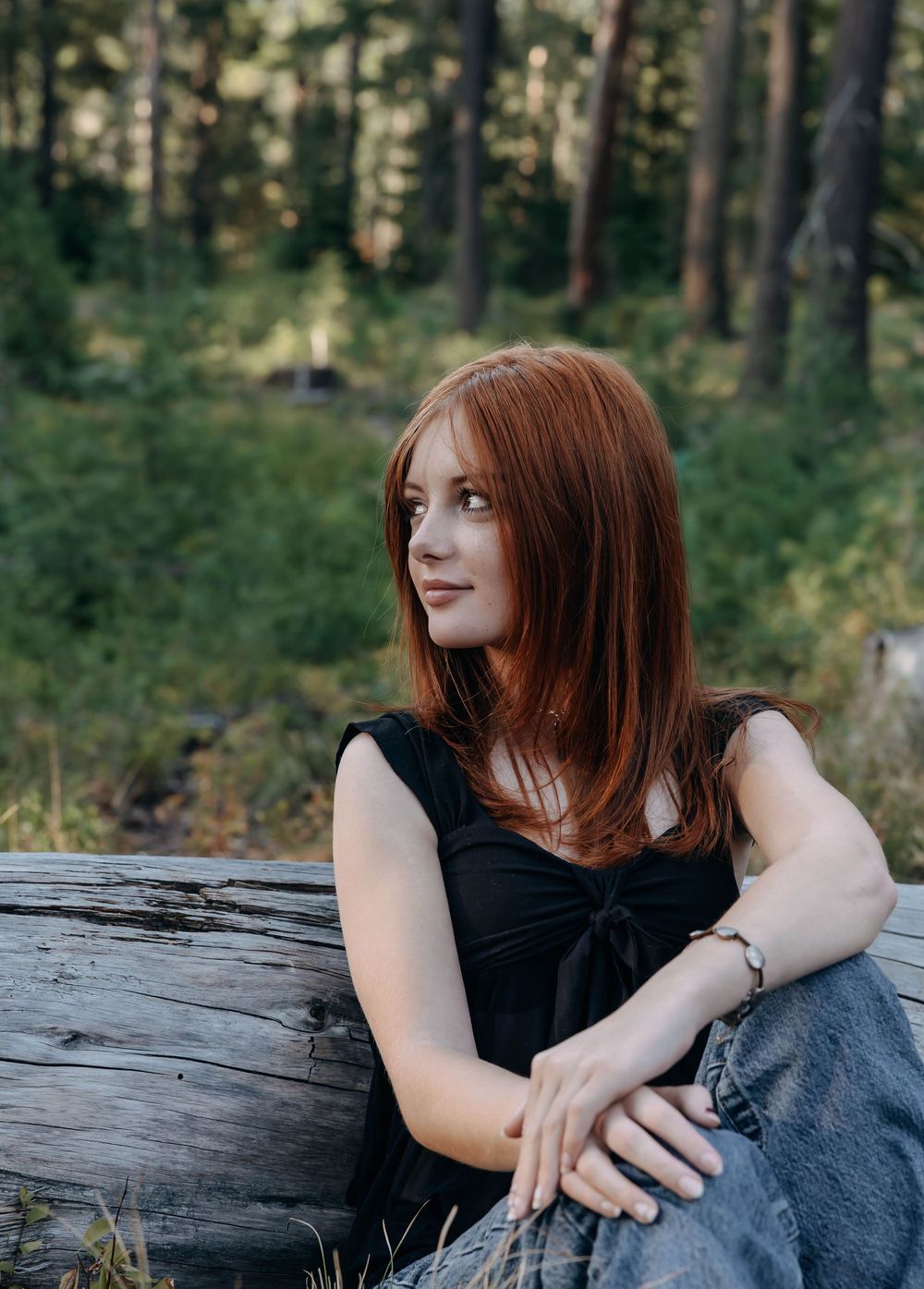 Person in black top relaxes on weathered log during forest photoshoot.