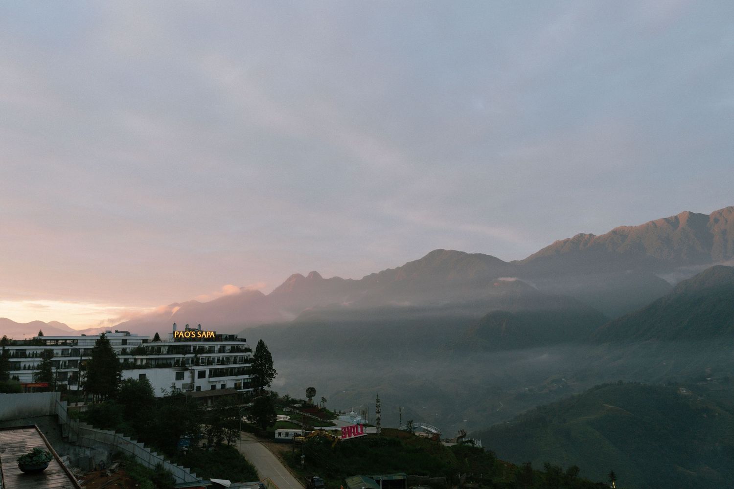 Misty mountain sunrise landscape with resort buildings and foggy valley below.