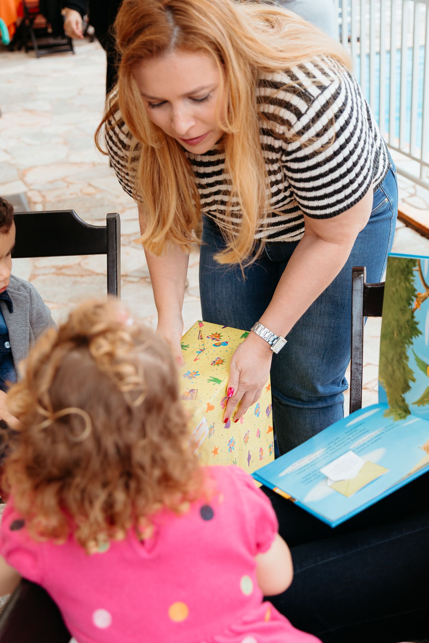 Reading time with a child in a polka dot dress while someone in striped shirt points to a blue book.