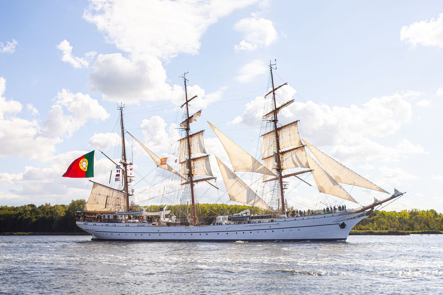 Majestic tall ship with white sails glides across the ocean waters against a cloudy sky backdrop.