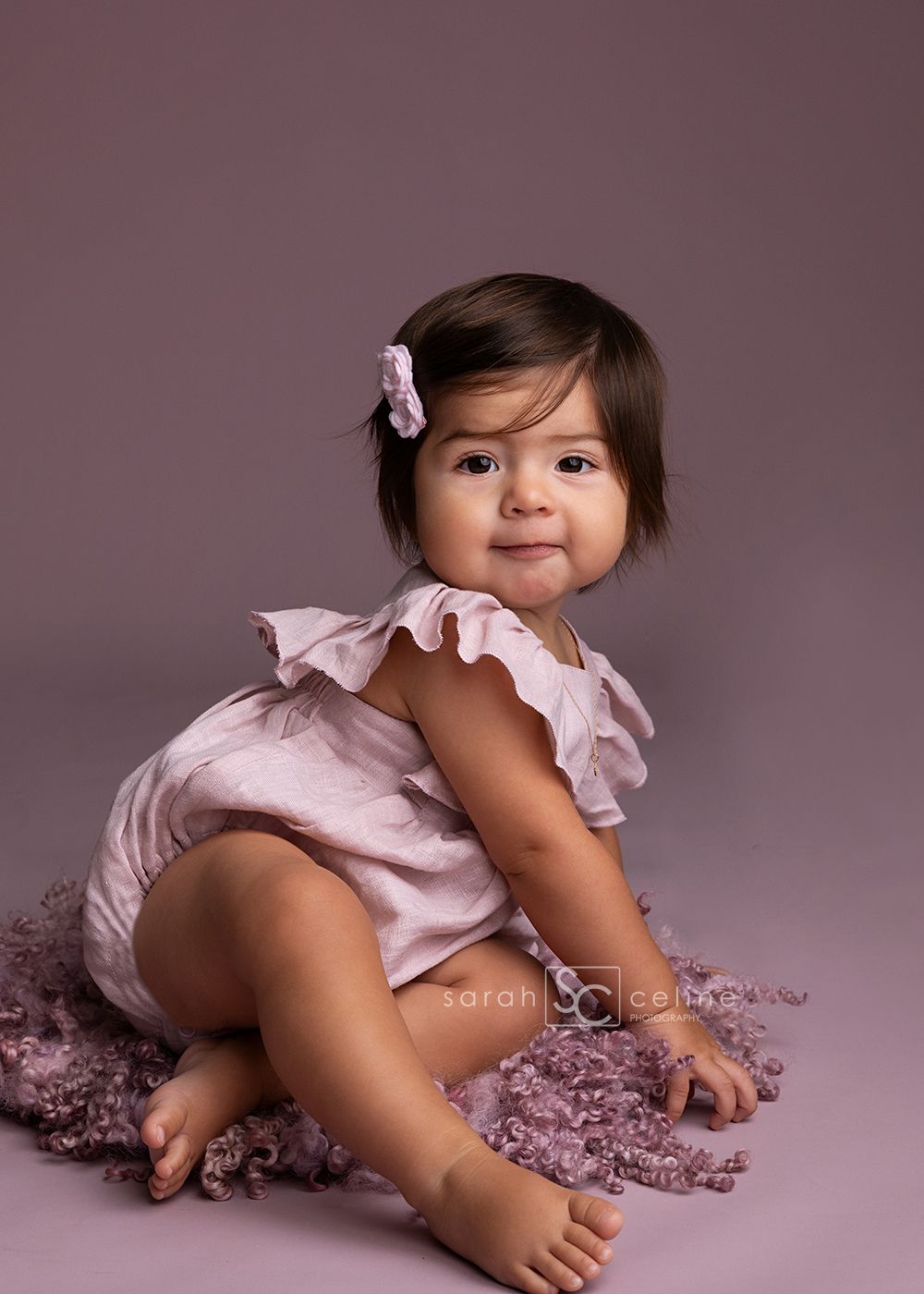A baby in a pink ruffled outfit crawls and plays on a soft pink backdrop in a series of connected photos.