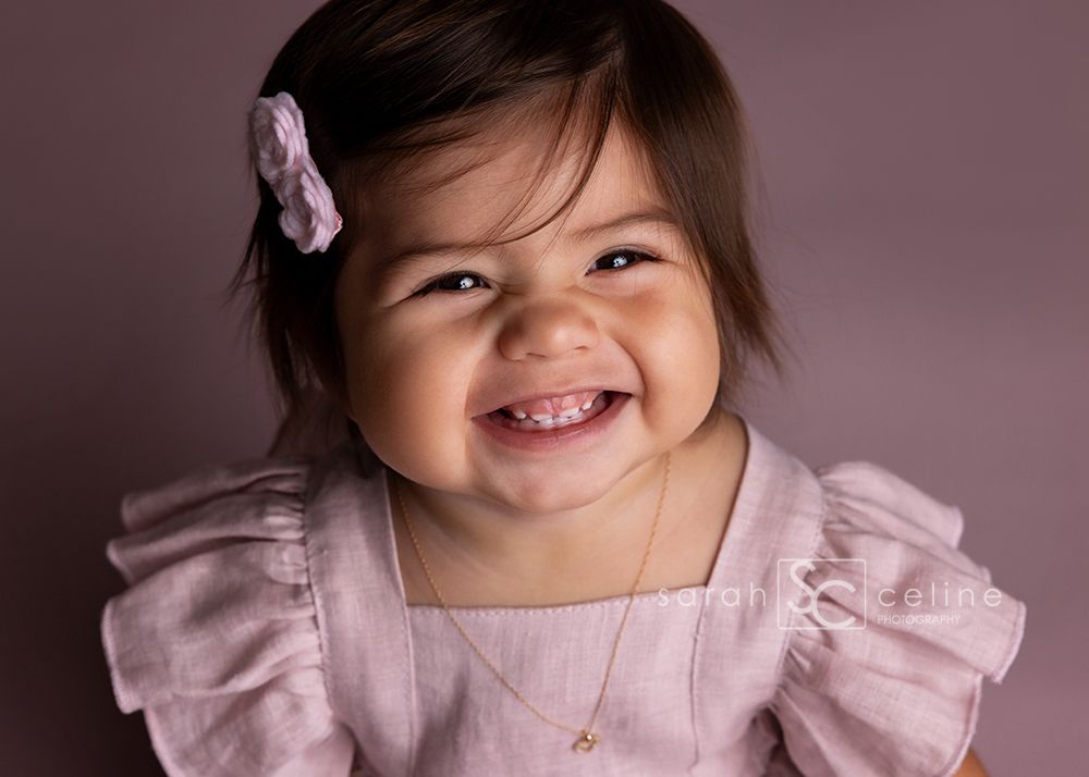 Close-up portrait shots of baby in pink dress against mauve background.