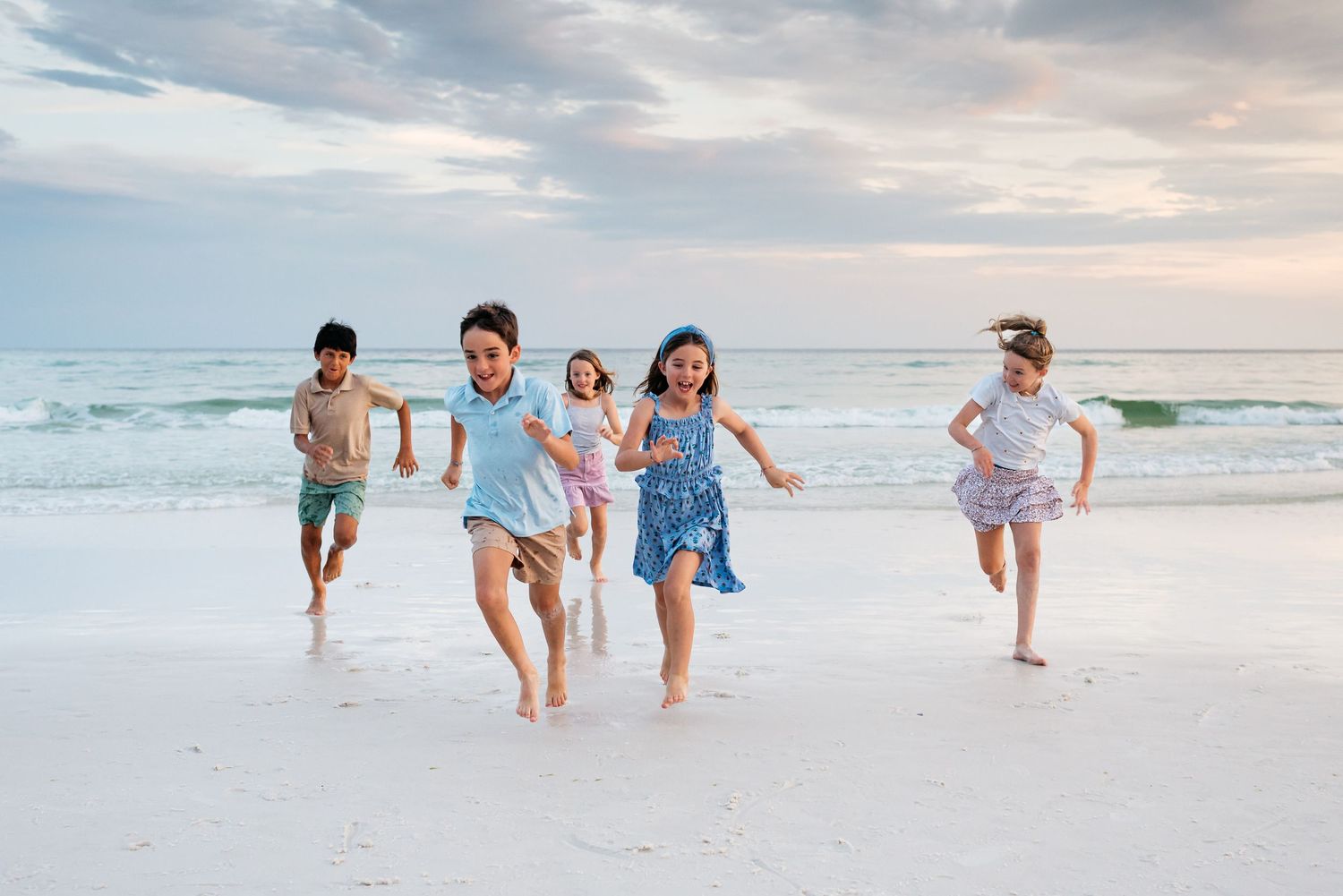 Children running and playing together along the shoreline at dusk with waves crashing behind them.