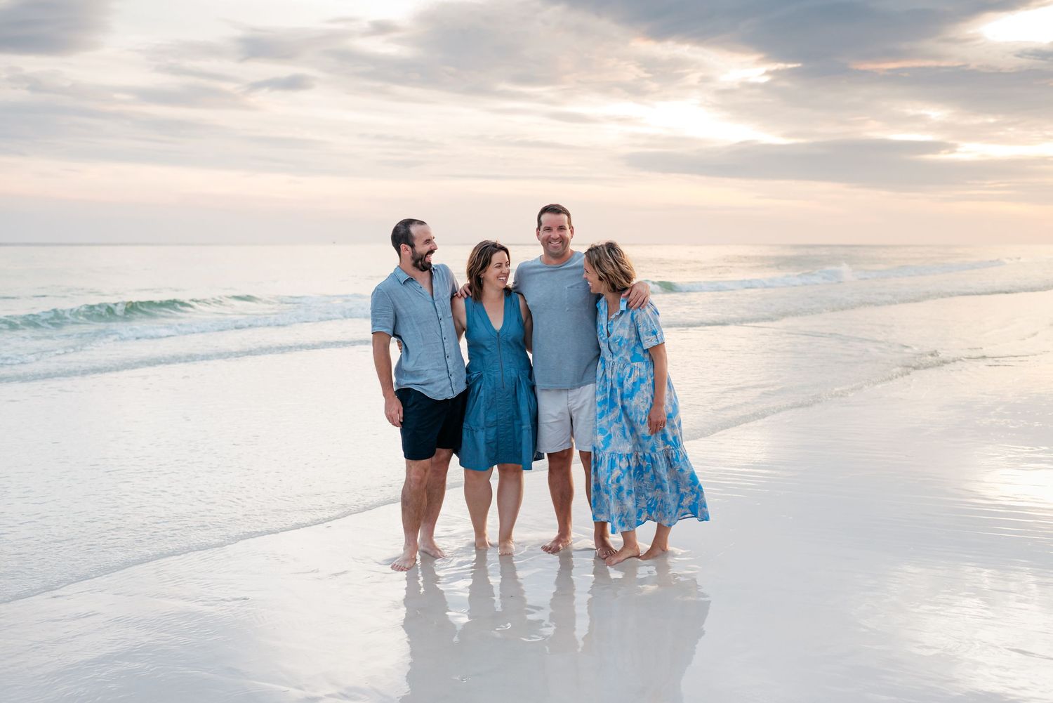 People in coordinating blue outfits walking along a beach shoreline at sunset.
