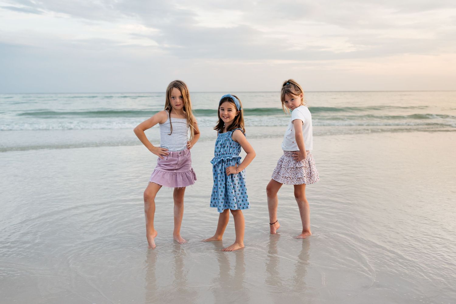 Kids in casual summer outfits playing and splashing at the beach during sunset.