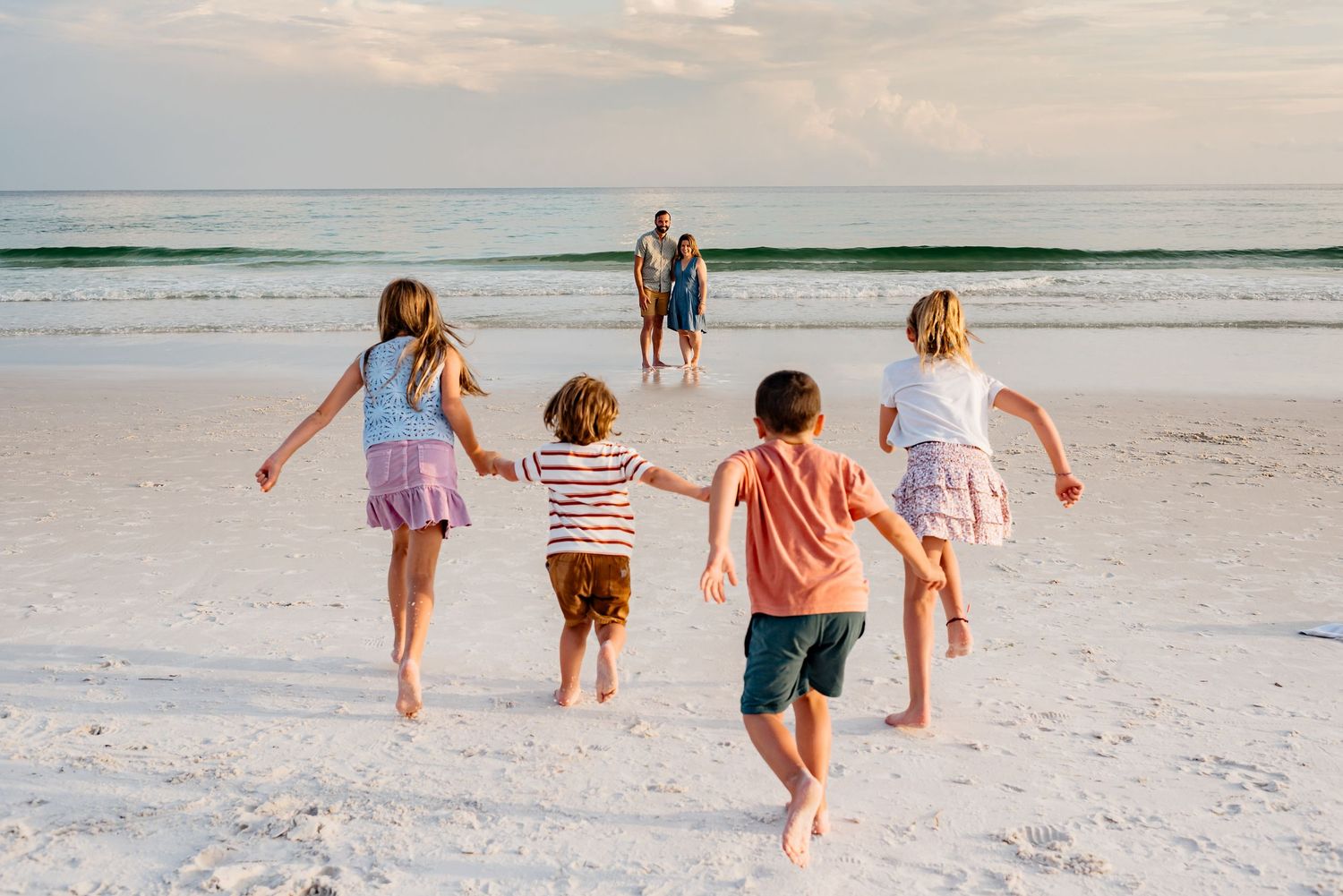 Family enjoys golden hour walk on white sandy beach with rolling waves in the background.