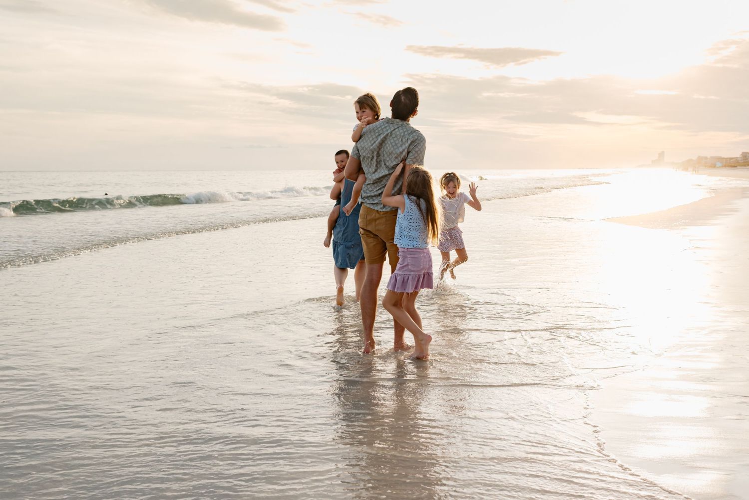 Several figures walk along a pristine beach shoreline at sunset while waves gently lap at their feet.
