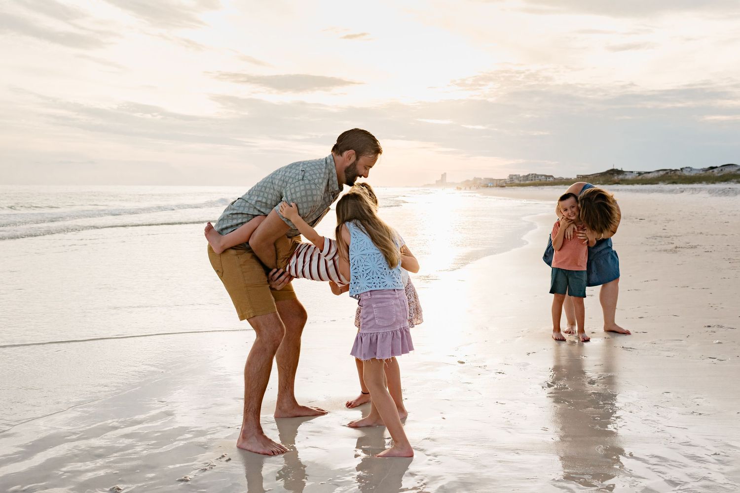 Family members walking and playing together on a sandy beach at sunset with ocean waves in the background.