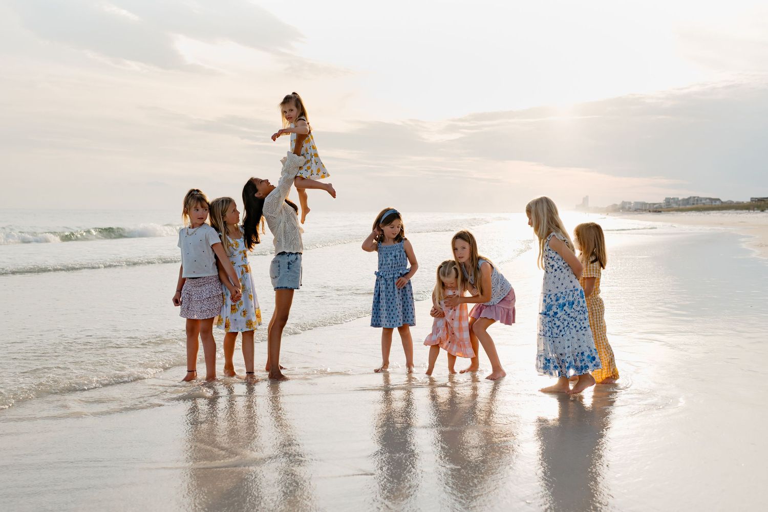 Groups of people explore and play along a serene white sandy beach during golden hour sunset.