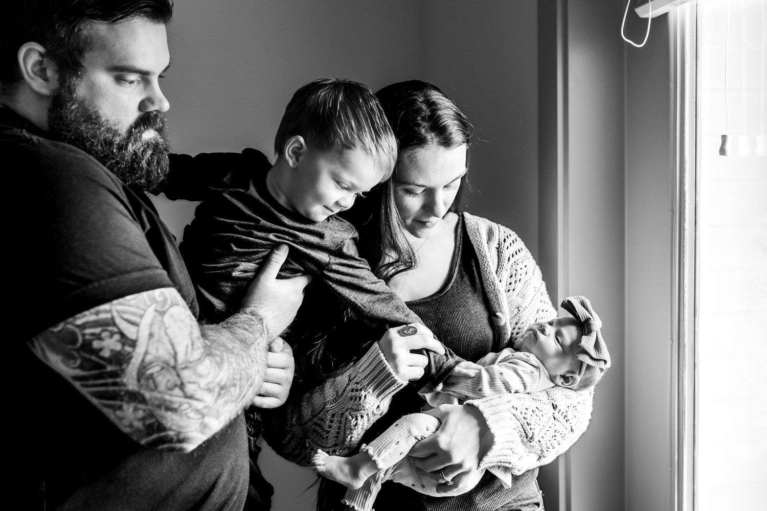 Black and white photo of a family loving on their new baby beside a window.
