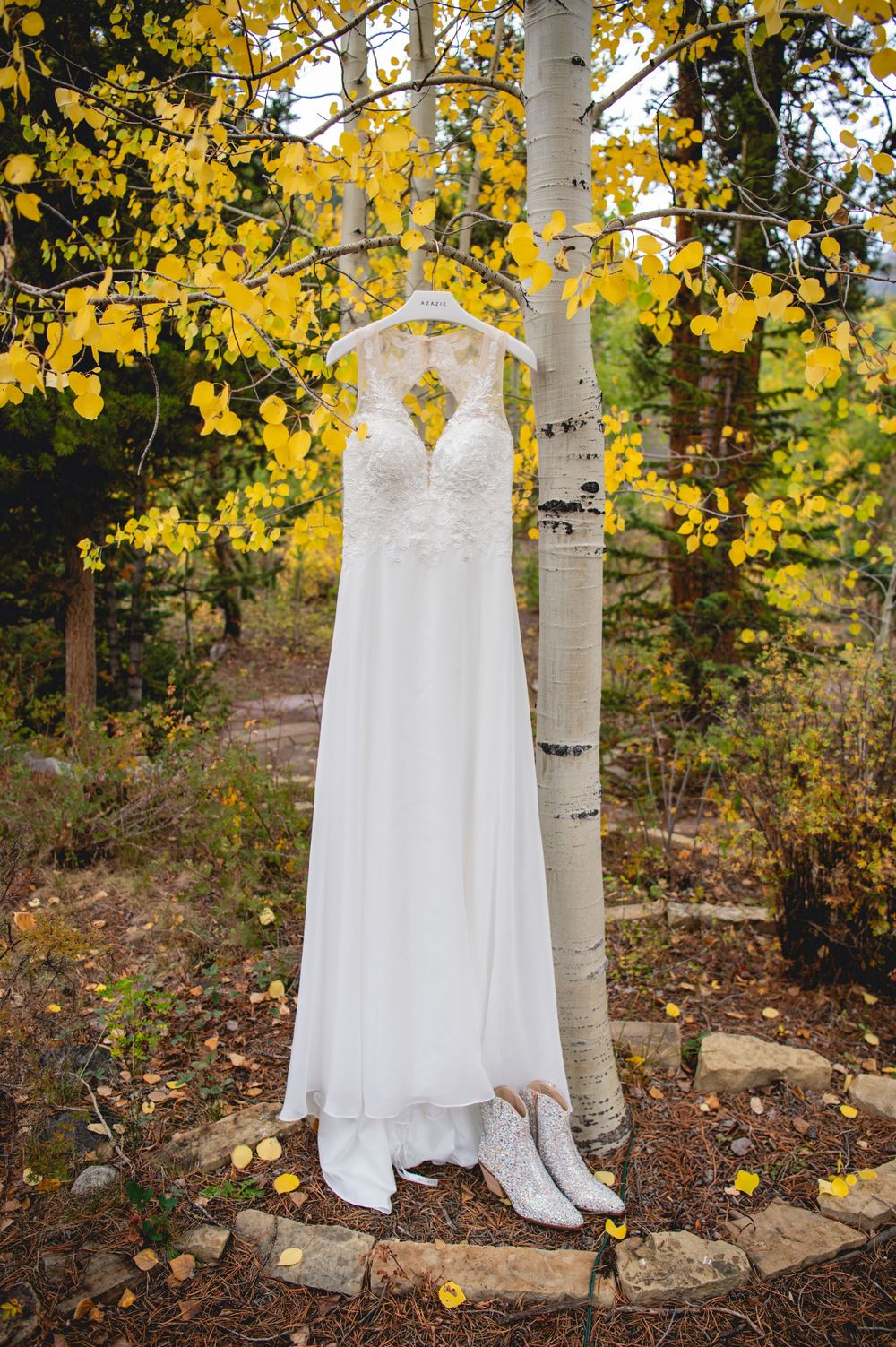 A white wedding dress hangs elegantly from an aspen tree with golden autumn leaves falling in the background.