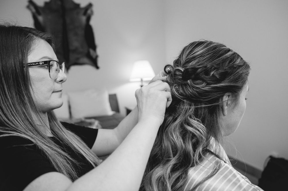 Hair stylist working on client's hair during wedding day preparation in black and white photography.