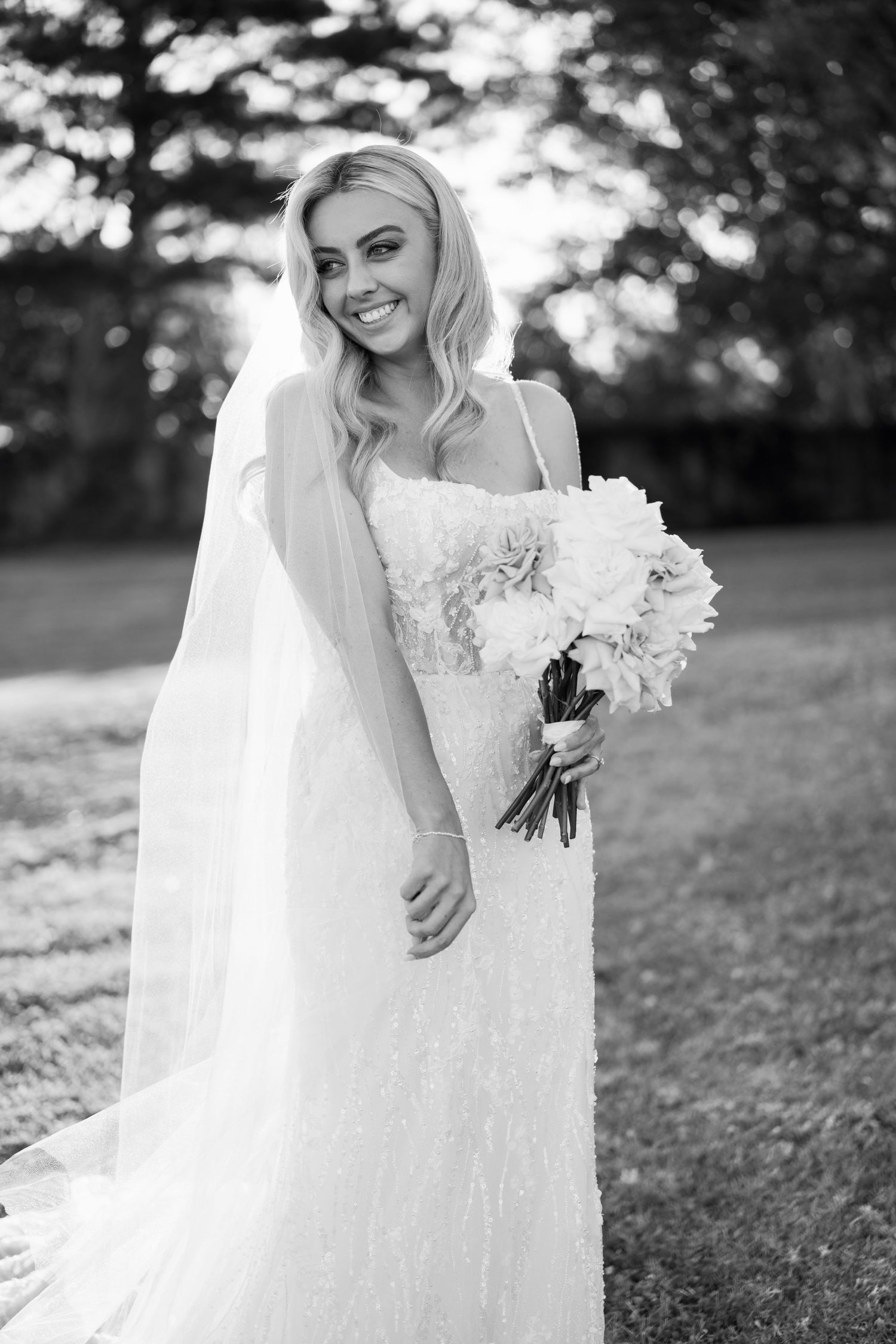 A stunning black and white wedding photo series showing a bride in a lace gown with a flowing veil in an outdoor garden setting.