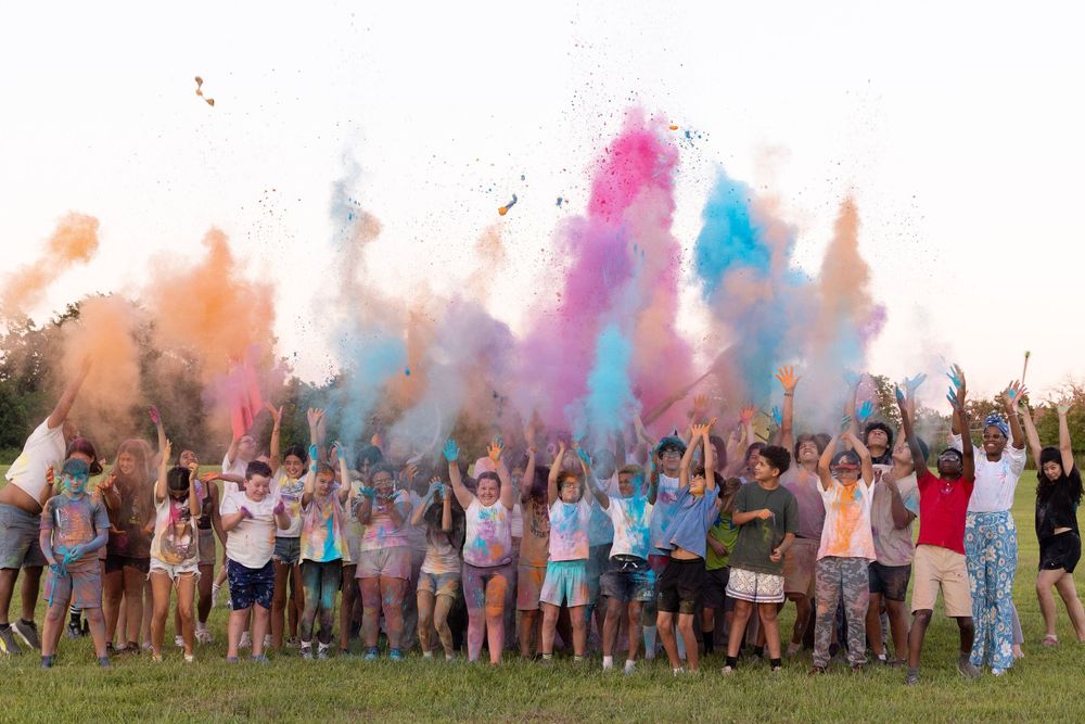 a crowd of children and youth throwing powdered color up in the air and smiling or yelling