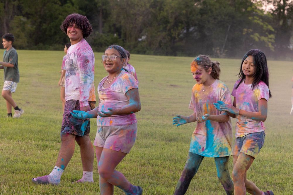 5 young people walking on a field, covered in colorful powder after a color war game