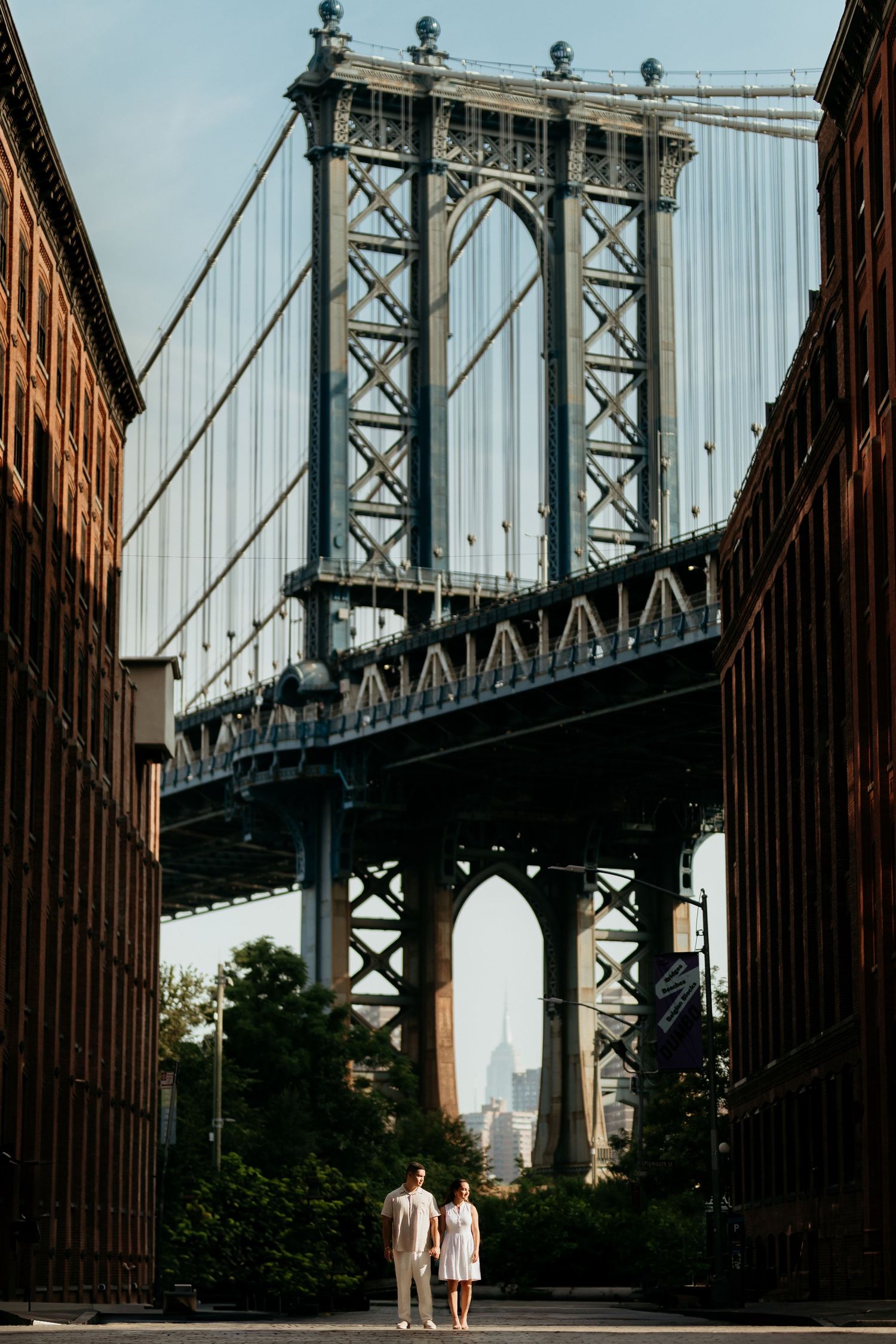 Manhattan Bridge spans the East River at sunset with the Empire State Building visible in the distance through its arches.
NY wedding photog