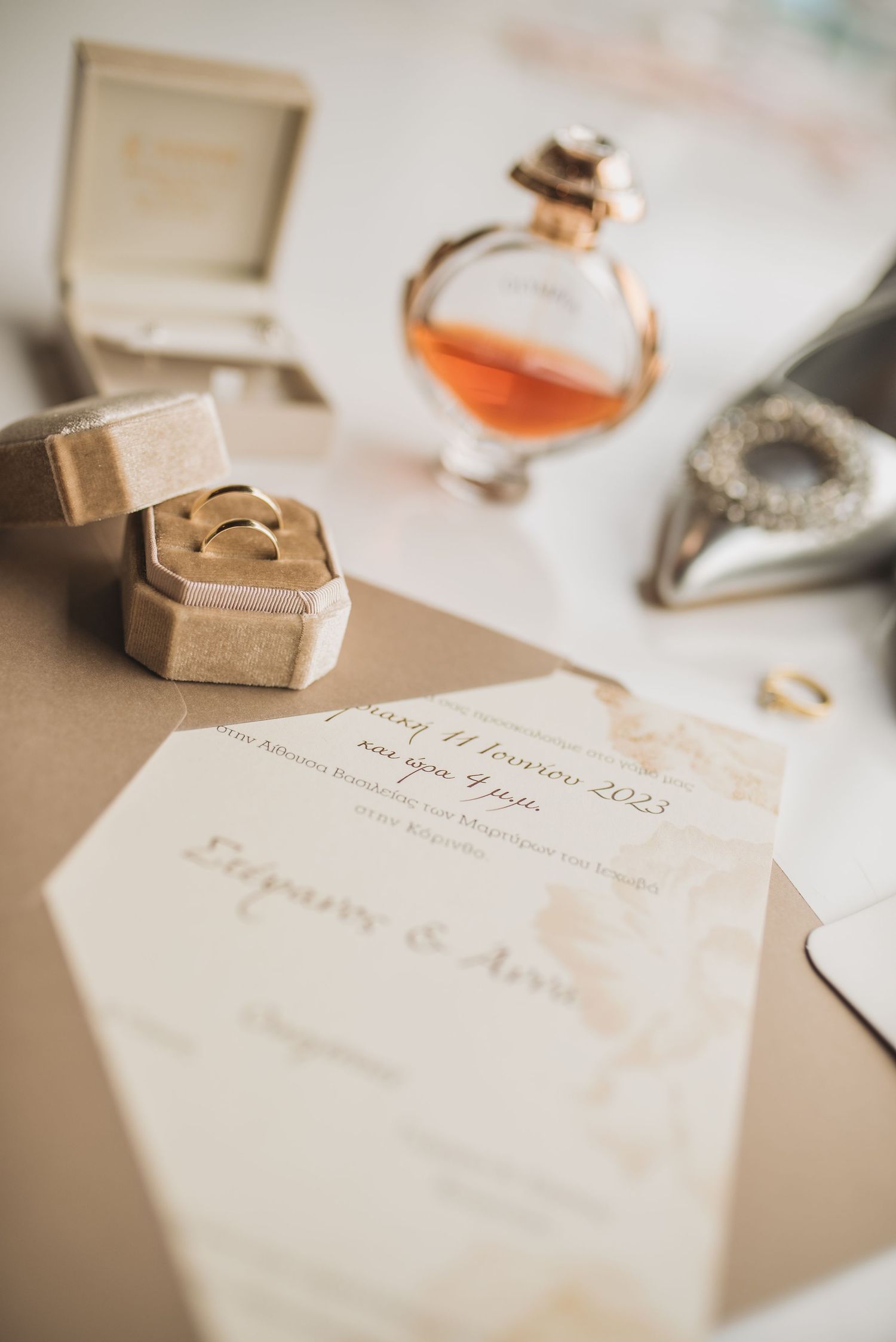 Wedding invitation suite with elegant calligraphy, rings and silver accessories arranged on a neutral background.