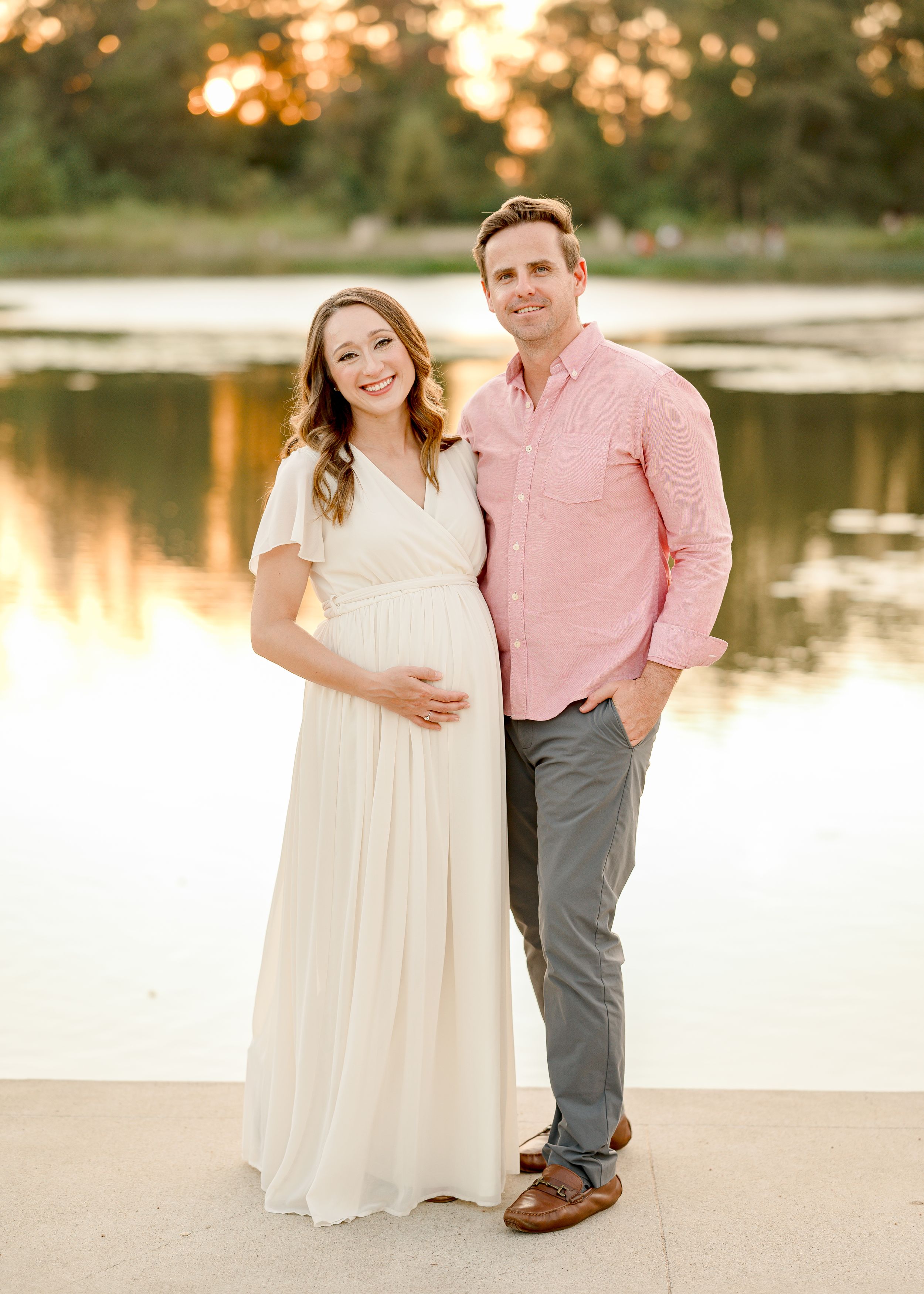 Expectant couple poses by lakeside during golden hour maternity shoot.