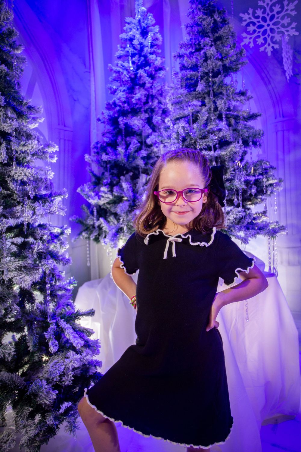 A festive indoor scene with purple-lit Christmas trees, snowflakes, and winter decorations creating a magical atmosphere.
