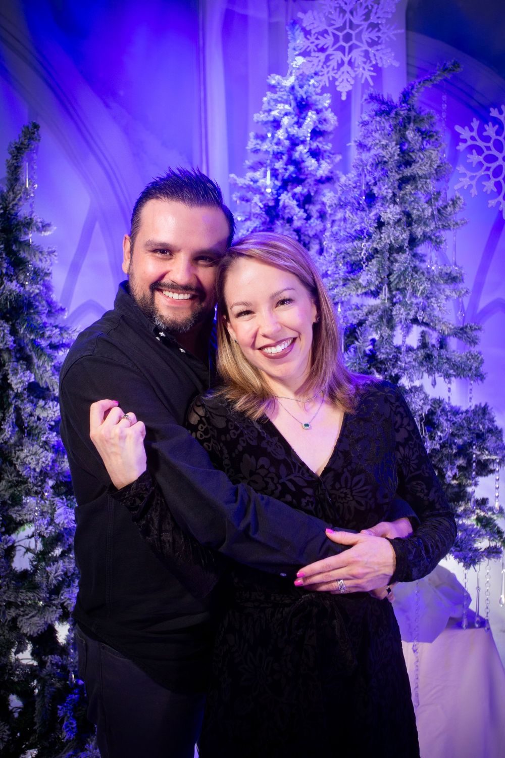 Couple poses playfully against a snow-covered winter wonderland backdrop with blue and purple lighting.