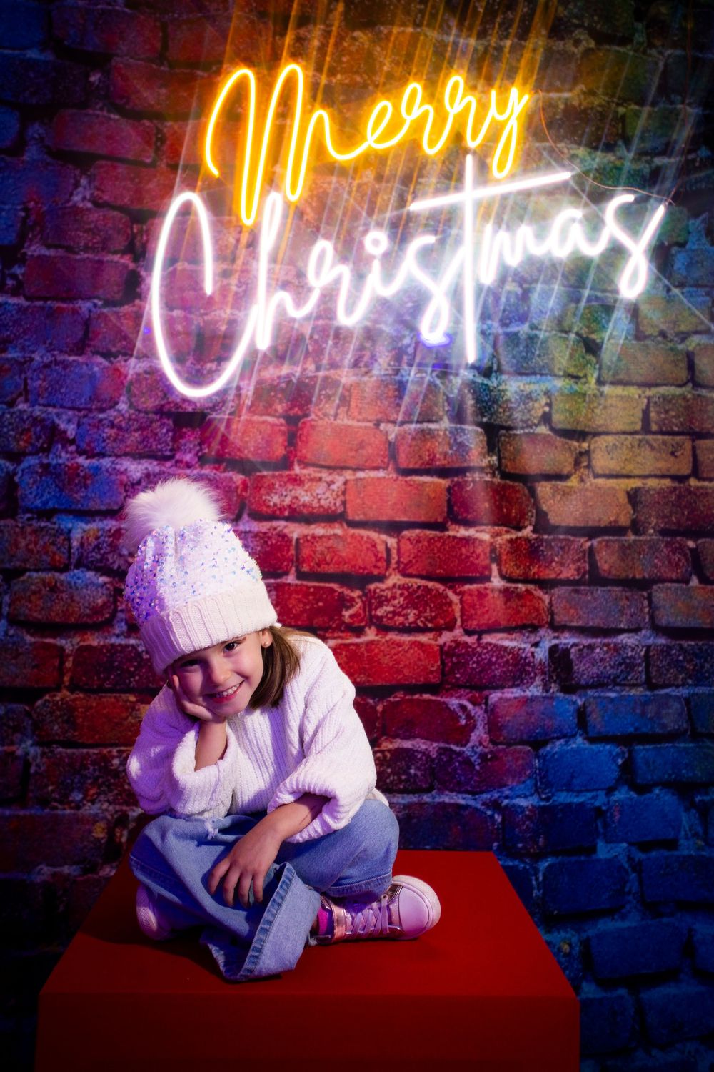 Figure in white winter clothing sits on red surface against exposed brick wall with illuminated neon sign above.