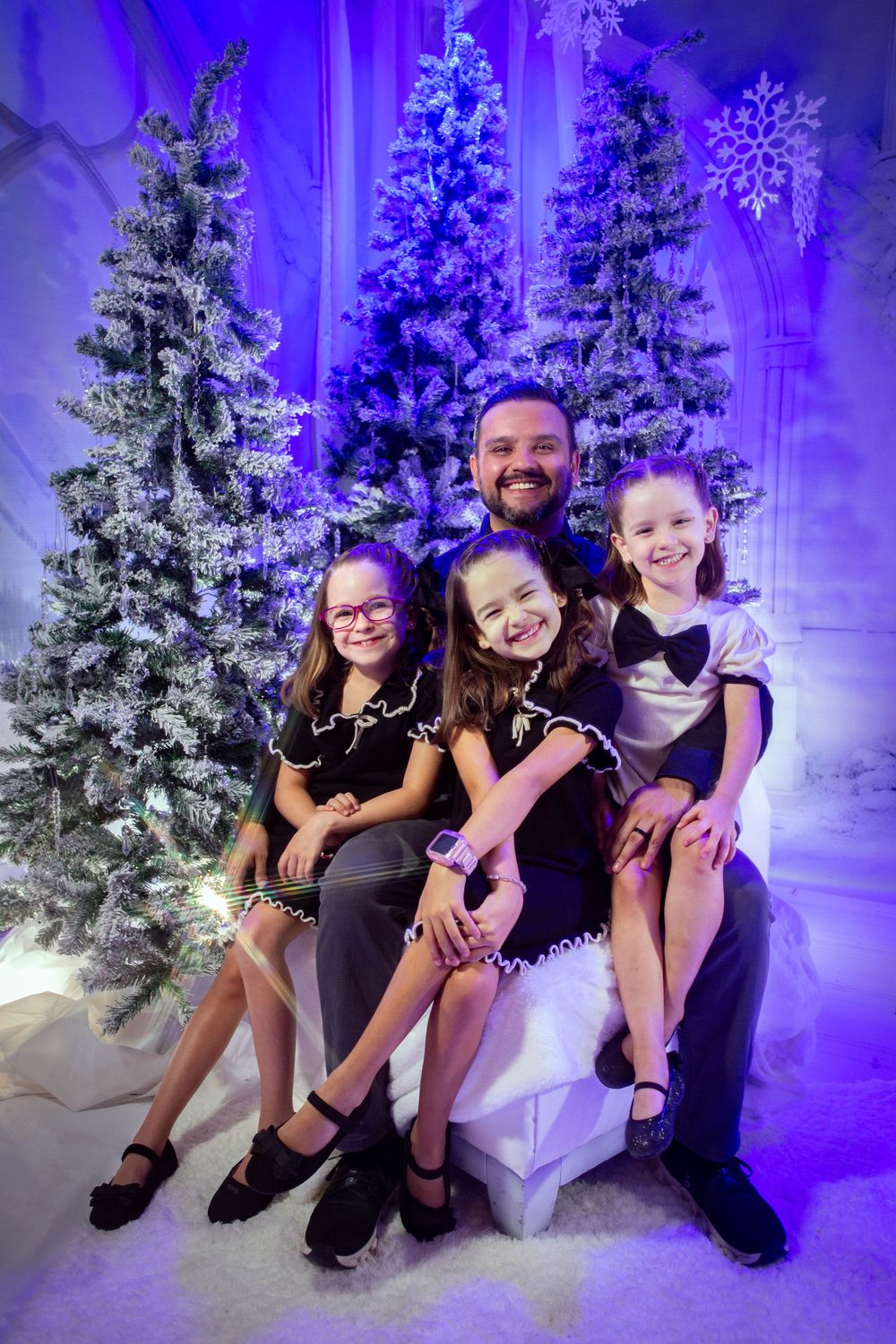 Several people seated together in front of snow-covered Christmas trees with blue lighting and decorations.