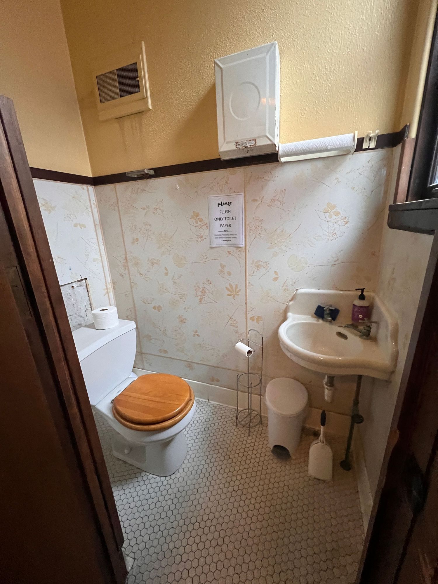 Compact bathroom with white fixtures, hexagonal floor tiles, and floral wallpaper accents.