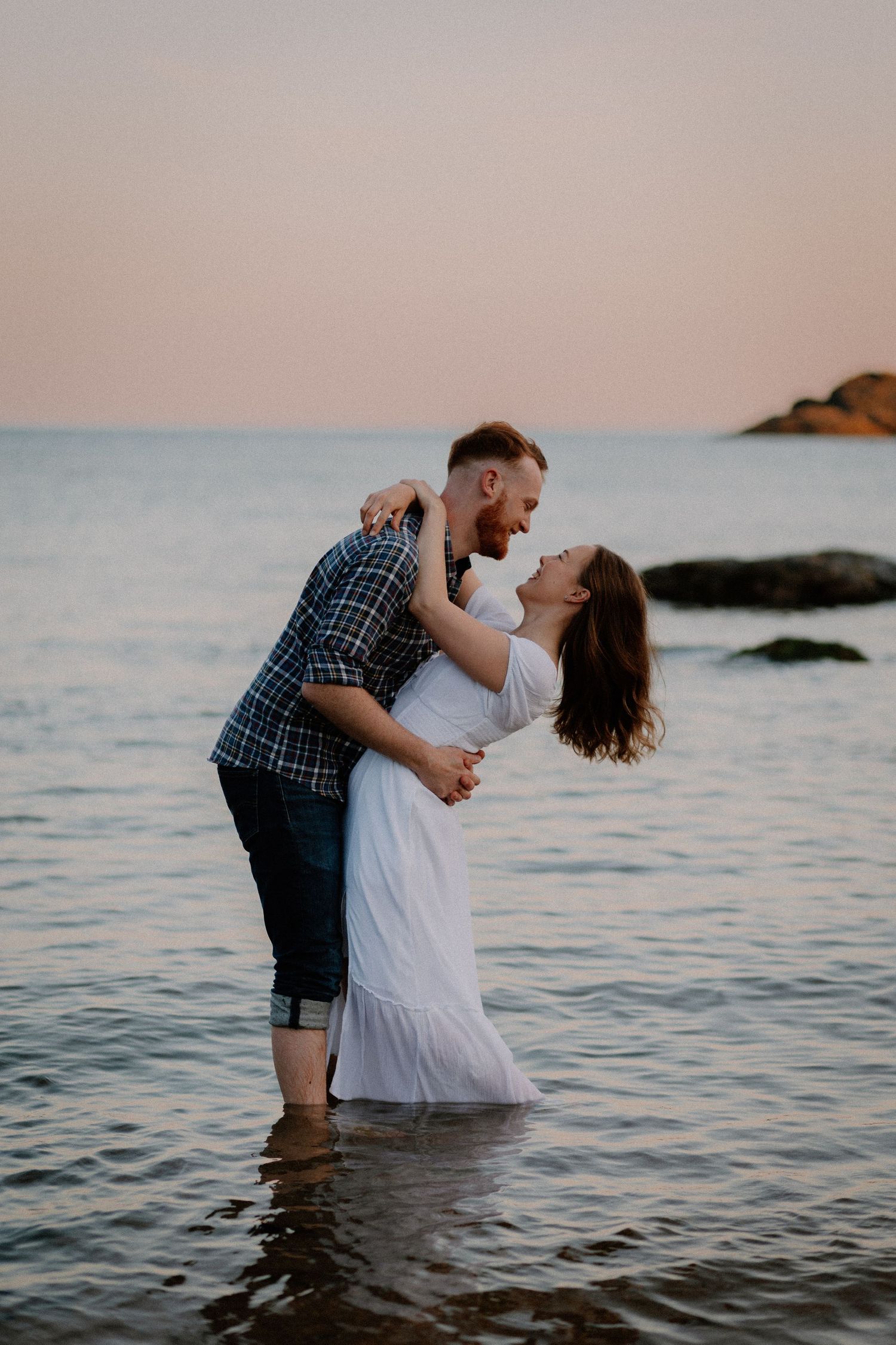 A romantic couple shares intimate moments while standing in the ocean water at sunset.