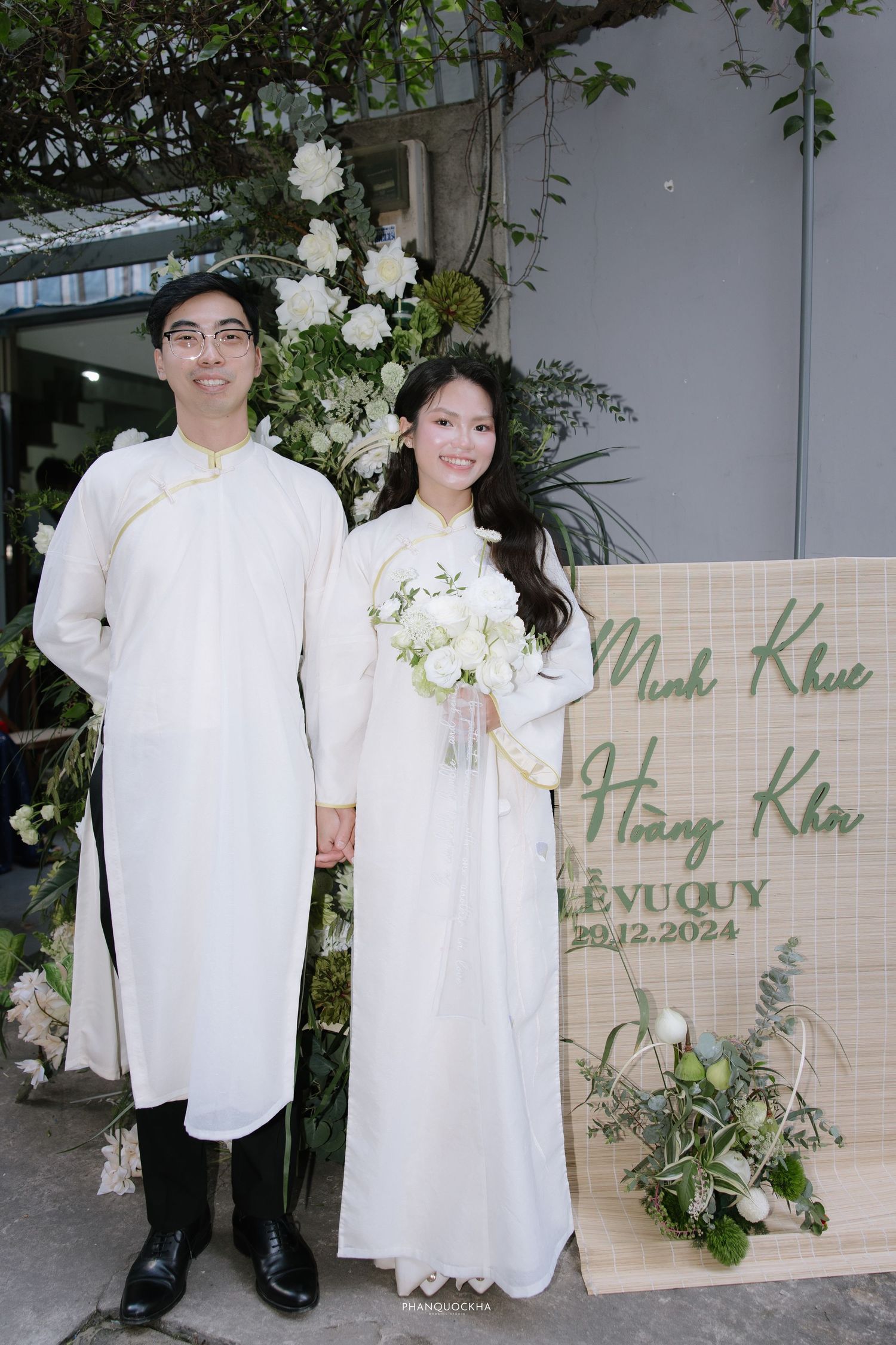Vietnamese couple in white ao dai pose by wedding sign for Minh Khue and Hoang Kha, December 2024.