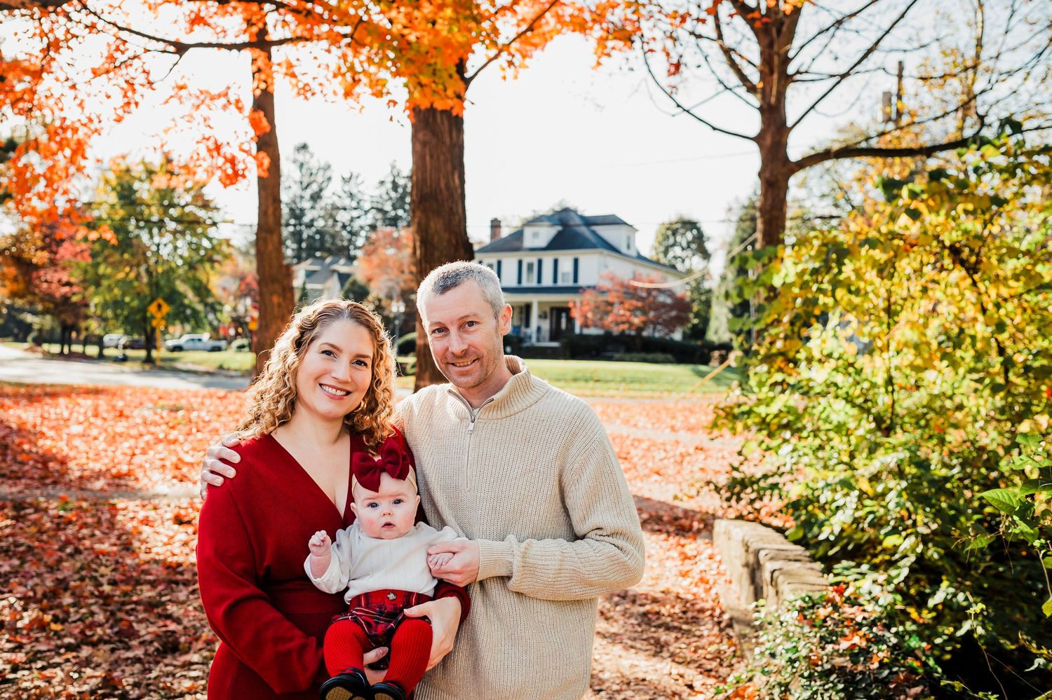 A family enjoys a sunny autumn day together surrounded by vibrant orange and yellow fall foliage in a park setting.